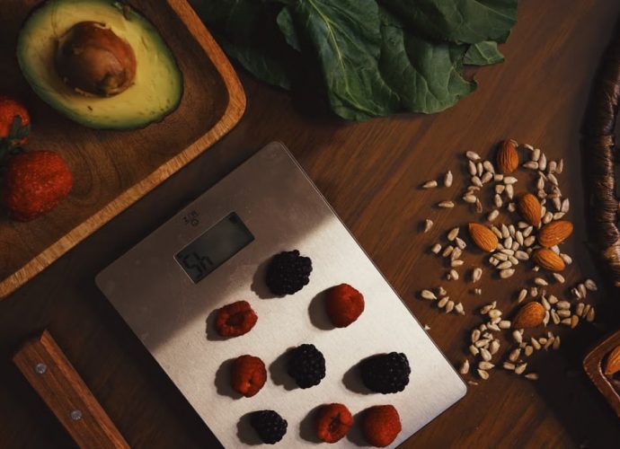 Top view of composed raw almond with seeds and avocado on table with berries on scales for cooking healthy dish