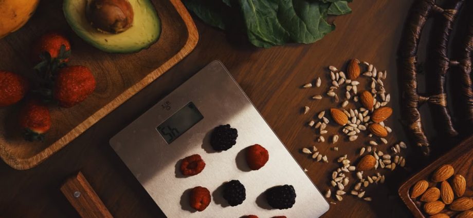 Top view of composed raw almond with seeds and avocado on table with berries on scales for cooking healthy dish